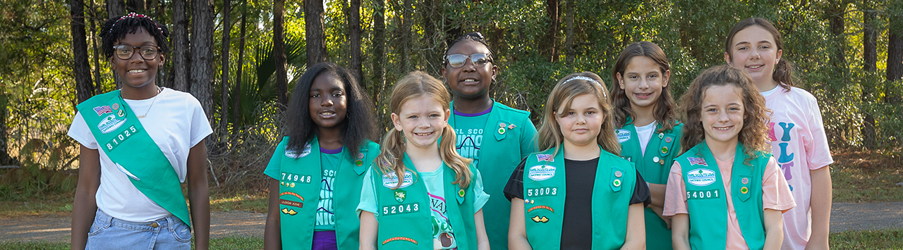  Two Girl Scouts standing on a sidewalk holding a sign that reads "Join Girl Scouts" 