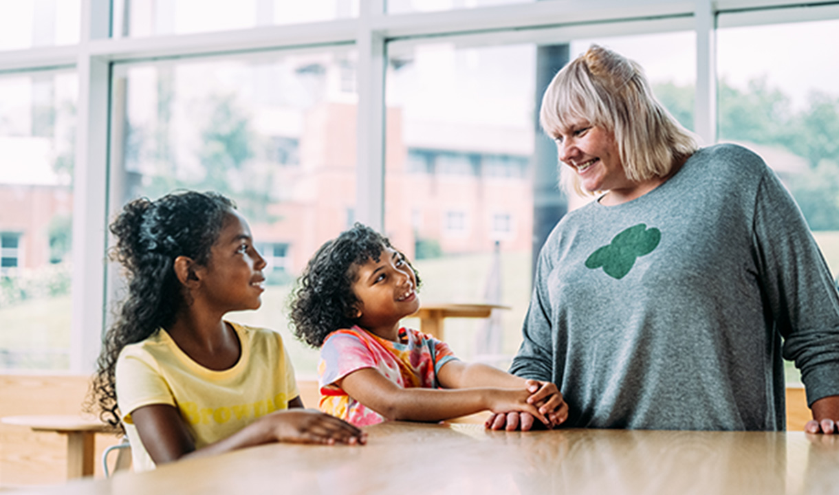 group of daisy girl scouts holding hands in uniform blue apron vest with patches and badges