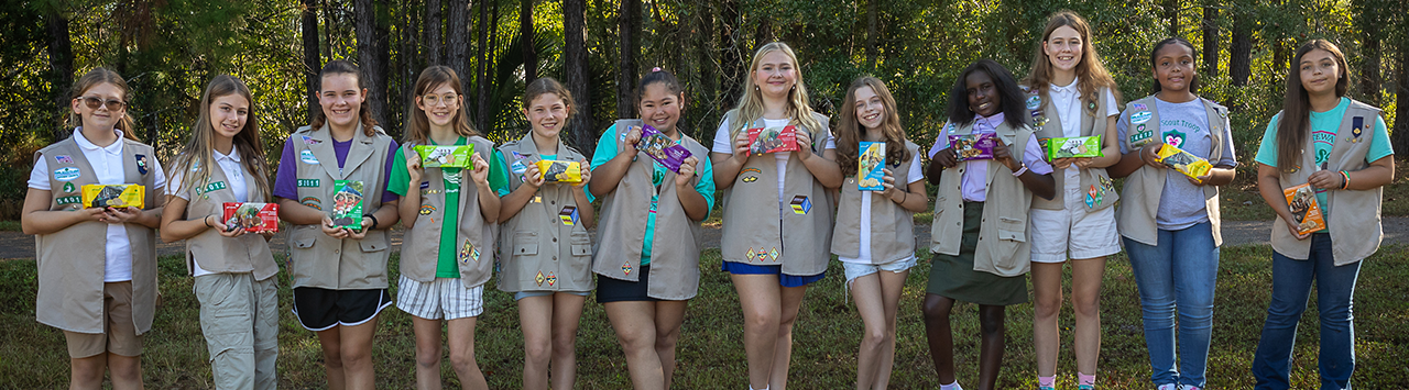  girl scout wearing uniform sash putting trefoil girl scout cookie boxes into cookie transport bag 