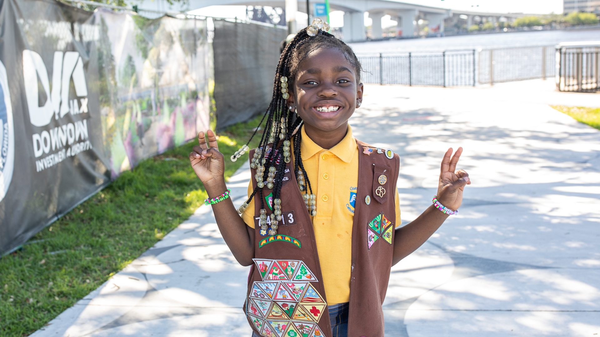 Brownie Girl Scout holding up peace sign in uniform at a park
